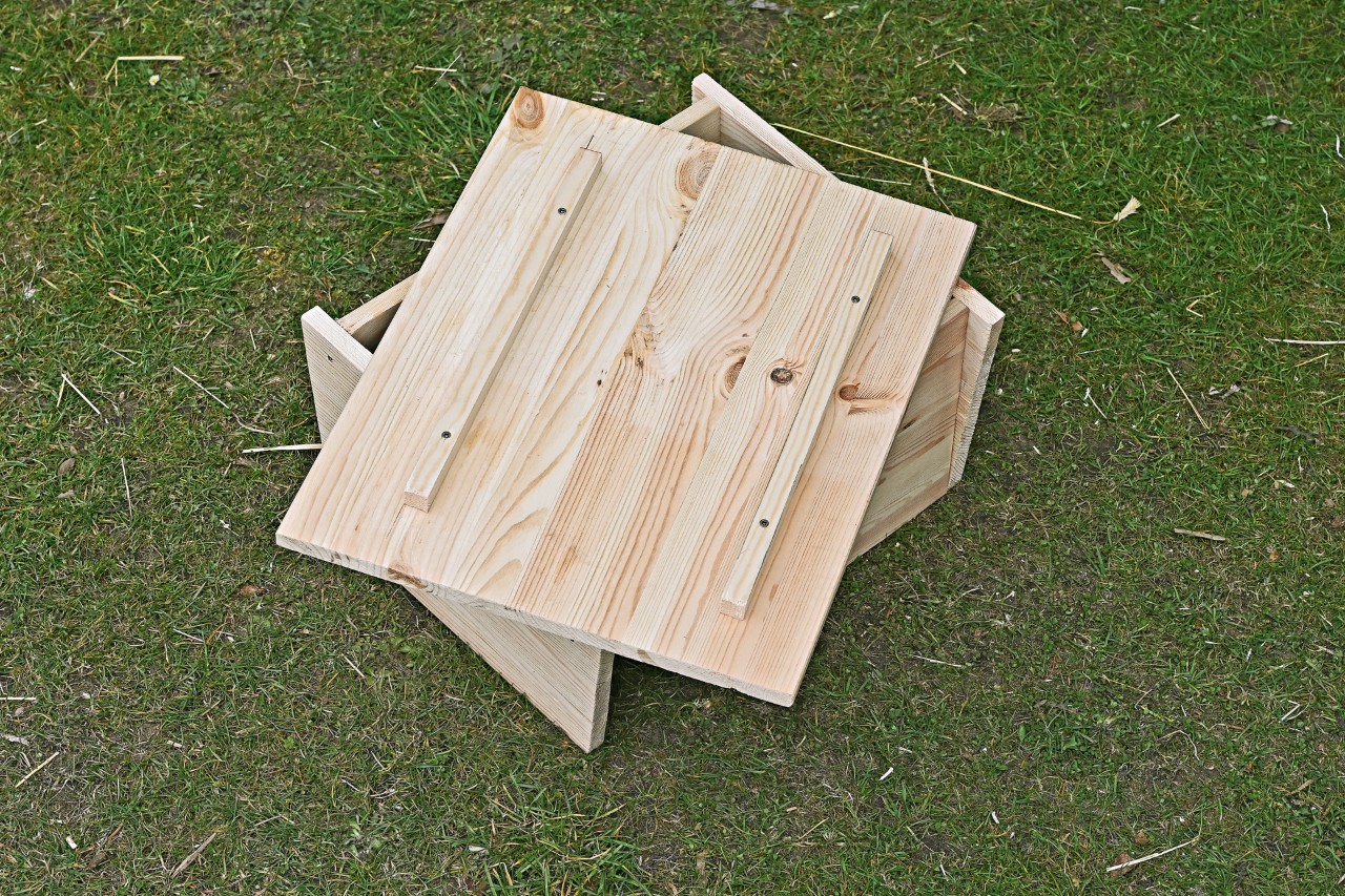 Eine Deckelplatte mit Holzleisten liegt lose auf einem Igelhaus zum Selberbauen