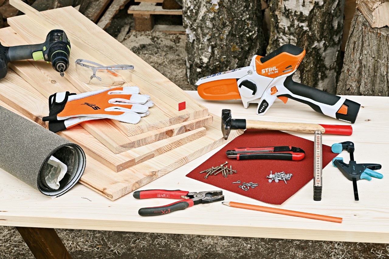 Materialien, um Igelhaus selber zu bauen: STIHL Akku-Gehölzschneider GTA 26, Holzplatten, Hammer, Nägel und weiteres Werkzeug
