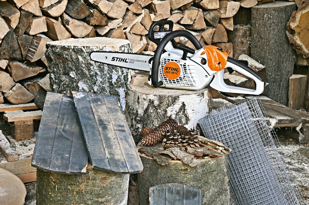 STIHL Benzin-Motorsäge MS 151 C auf einem Baumstumpf vor einem Holzstapel