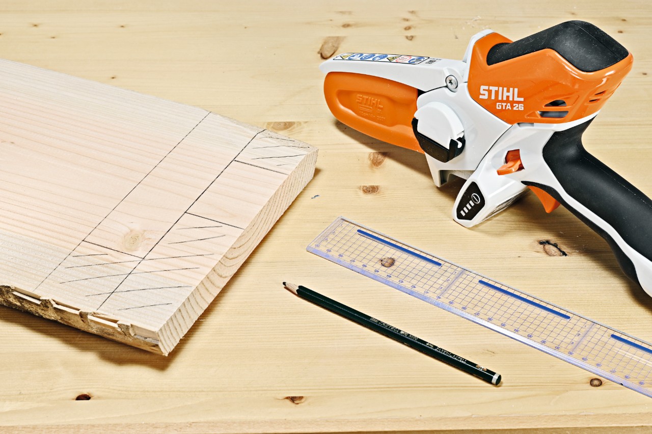 Bleistiftzeichnungen auf einer Holzbohle, daneben ein STIHL Akku-Gehölzschneider GTA 26