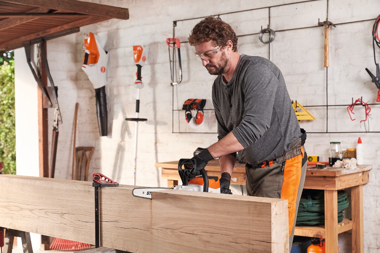 Mann mit Schutzausrüstung in Werkstatt beim Schneiden einer Holzbohle mit der STIHL Akku-Motorsäge MSA 140 C