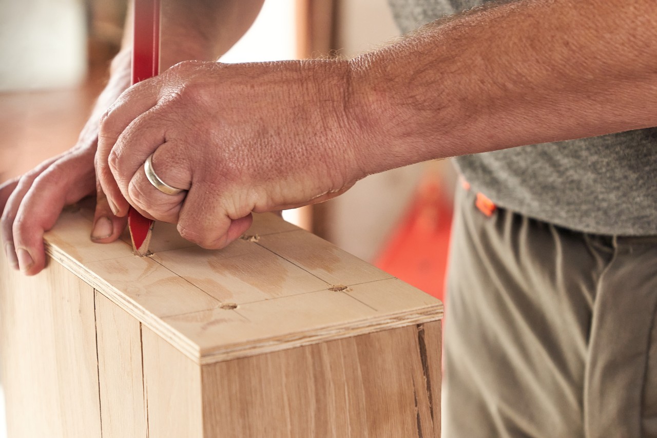 Mann markiert Bohrstellen auf einem Holzbalken mit Hilfe einer Bohrschablone