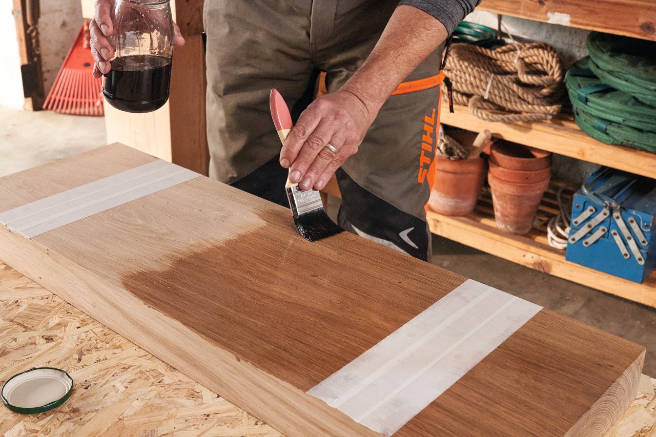 Mann mit STIHL Schnittschutzhose ölt einen Holzbalken mit einem Pinsel ein