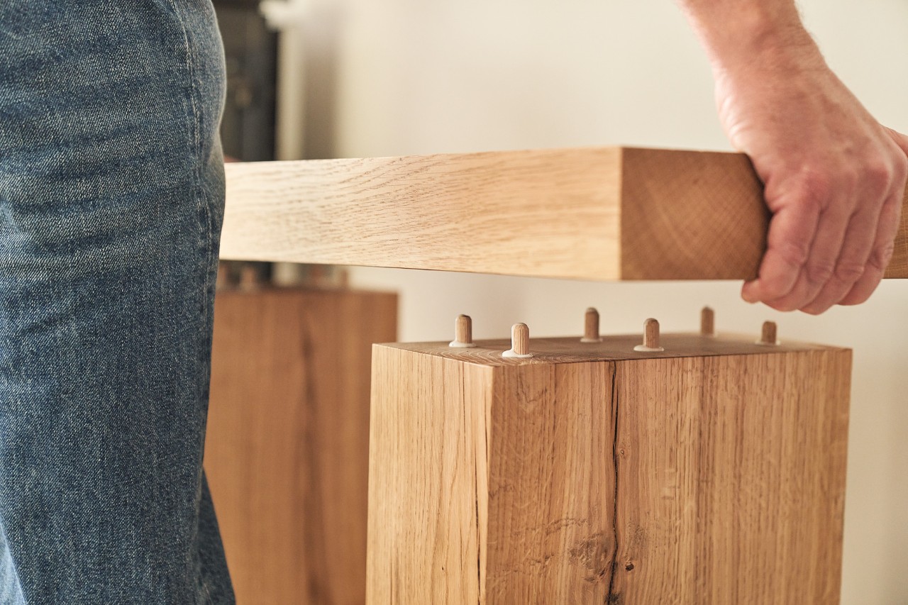Person steckt eine Holzbohle mit Hilfe von Dübeln auf Holzbalken