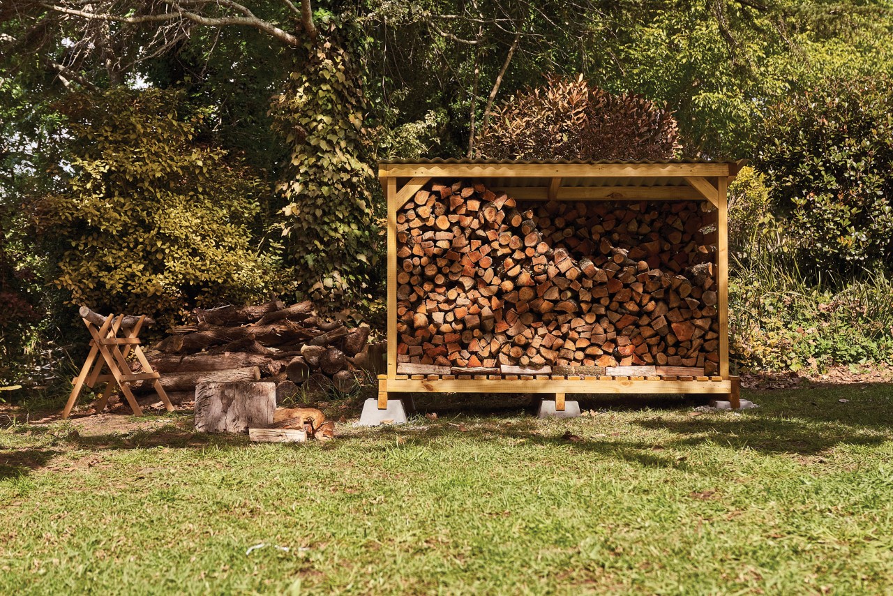 Mit Holzscheiten gefüllter Brennholzunterstand im Garten