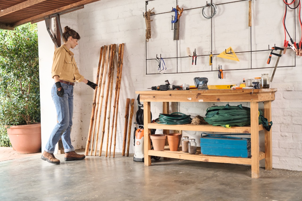 Eine Frau stellt die entrindeten Hölzer für den selber gebauten Kleiderständer zum Trocknen in die Garage