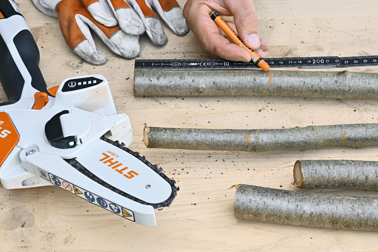 Geeignete Längenabschnitte werden an Ästen mit einem orangefarbenen Stift markiert, daneben liegen Schutzhandschuhe und der Akku-Gehölzschneider STIHL GTA 26 