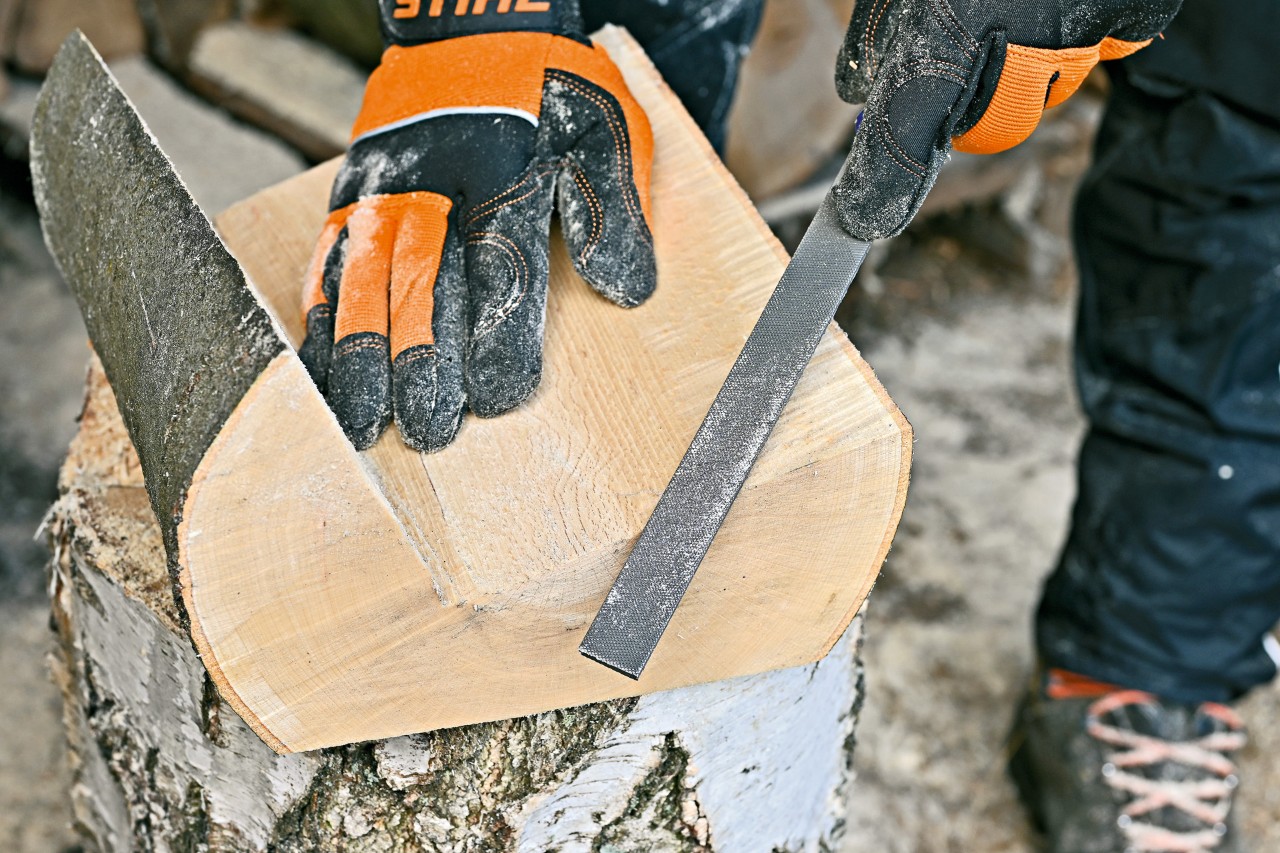 Person glättet die Kanten und Oberflächen eines Zeitungsständers aus Holz mit einer Metallfeile