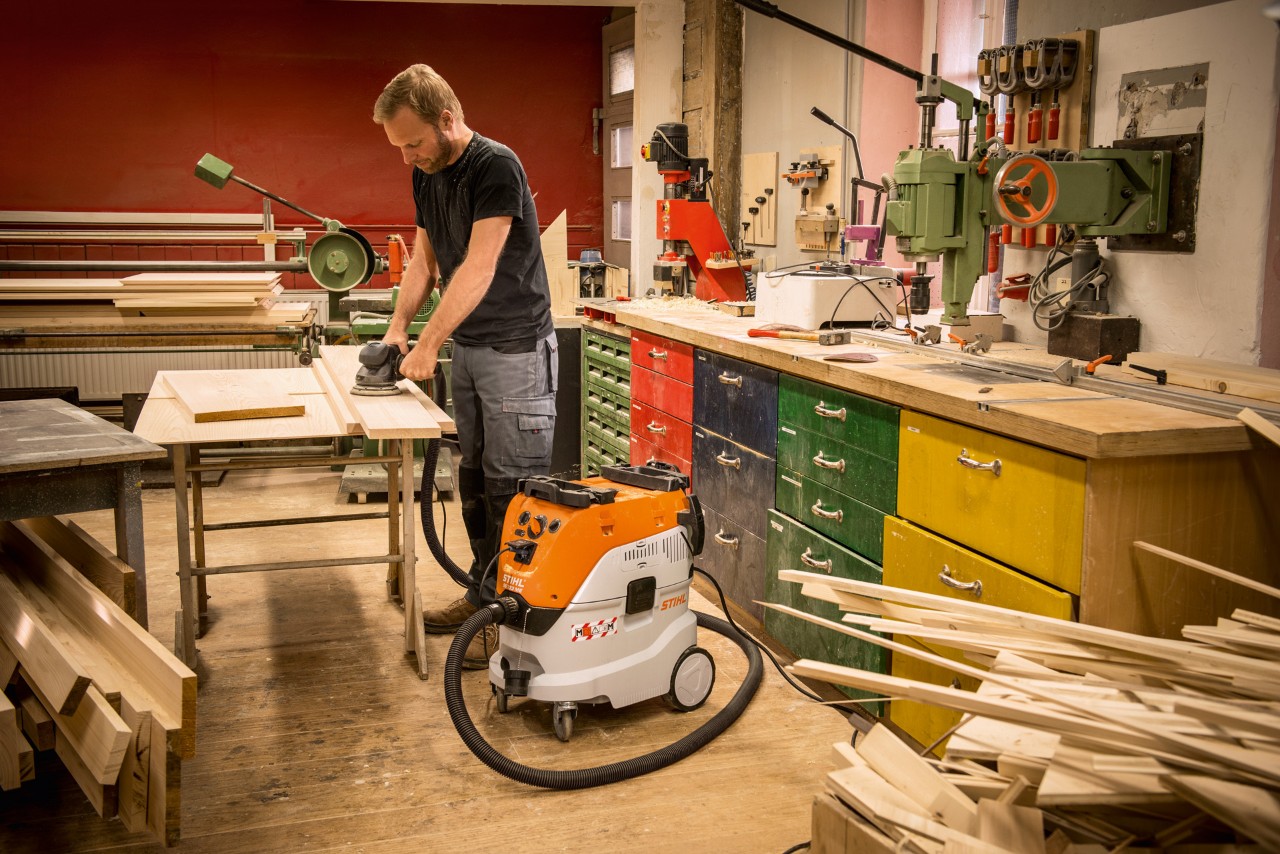 Mann nutzt STIHL Nass- und Trockensauger SE 133 ME in einer Werkstatt bei der Arbeit mit Holzbrettern