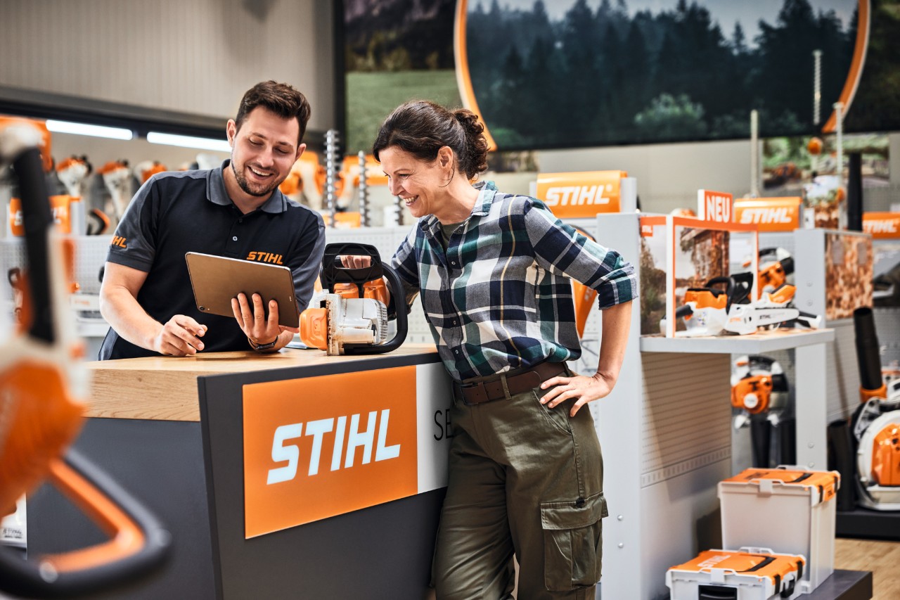 STIHL Fachhändler berät junge Frau bei Kauf einer STIHL Motorsäge vor einer Verkaufstheke