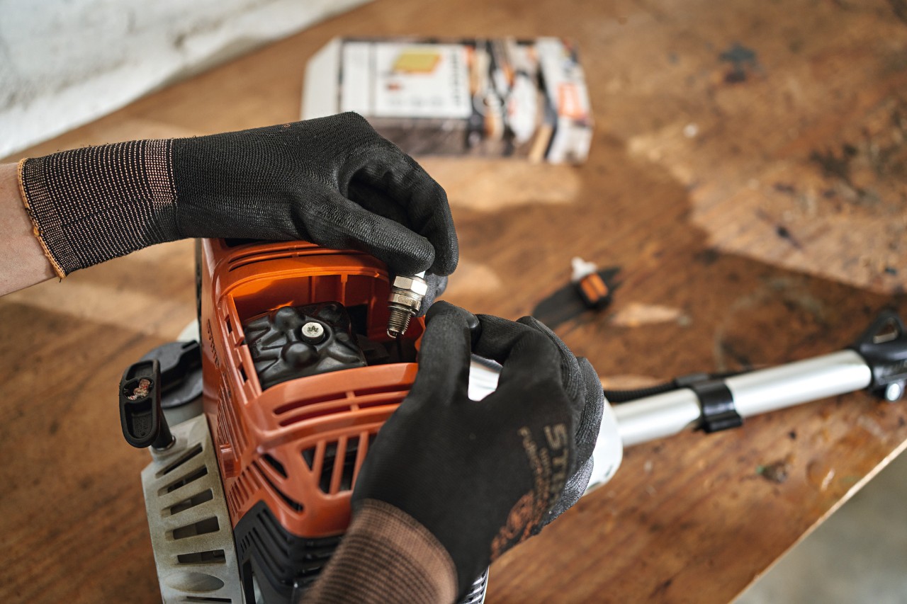 Nahaufnahme, wie an einem STIHL Benzin-Heckenschneider die Zündkerze ausgetauscht wird