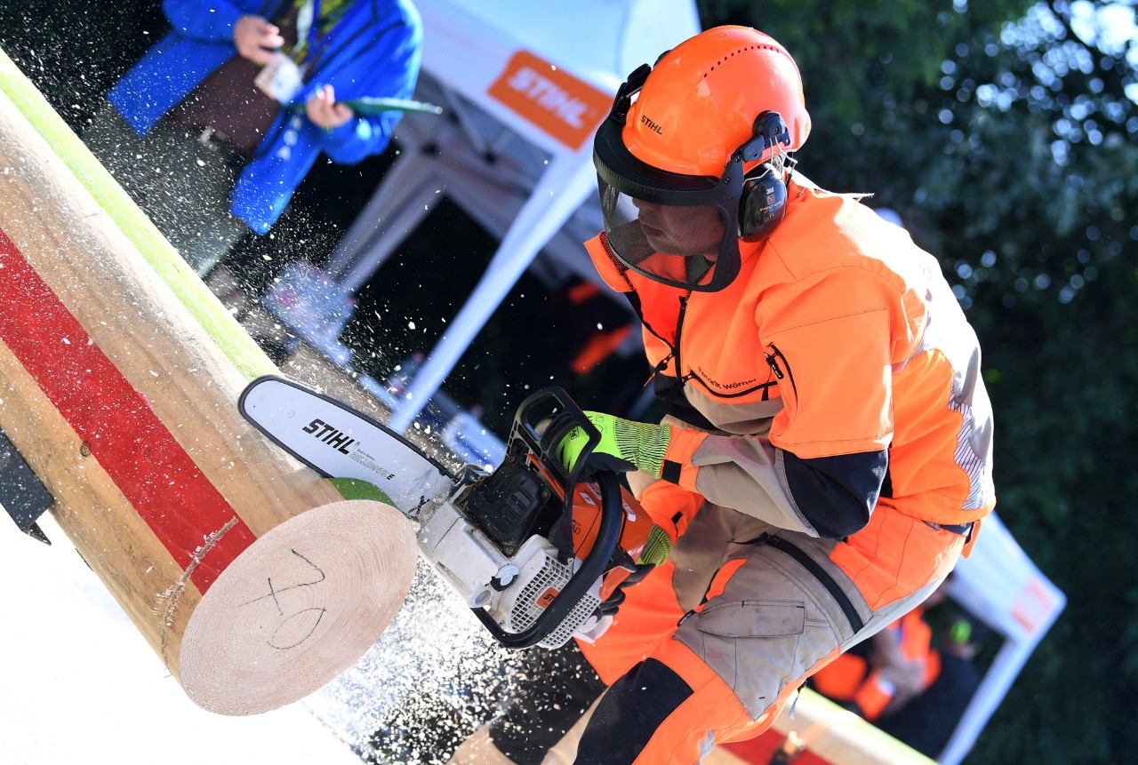 Schüler mit STIHL Kettensäge zersägt einen Baumstamm, im Hintergrund ein Zelt mit STIHL Logo