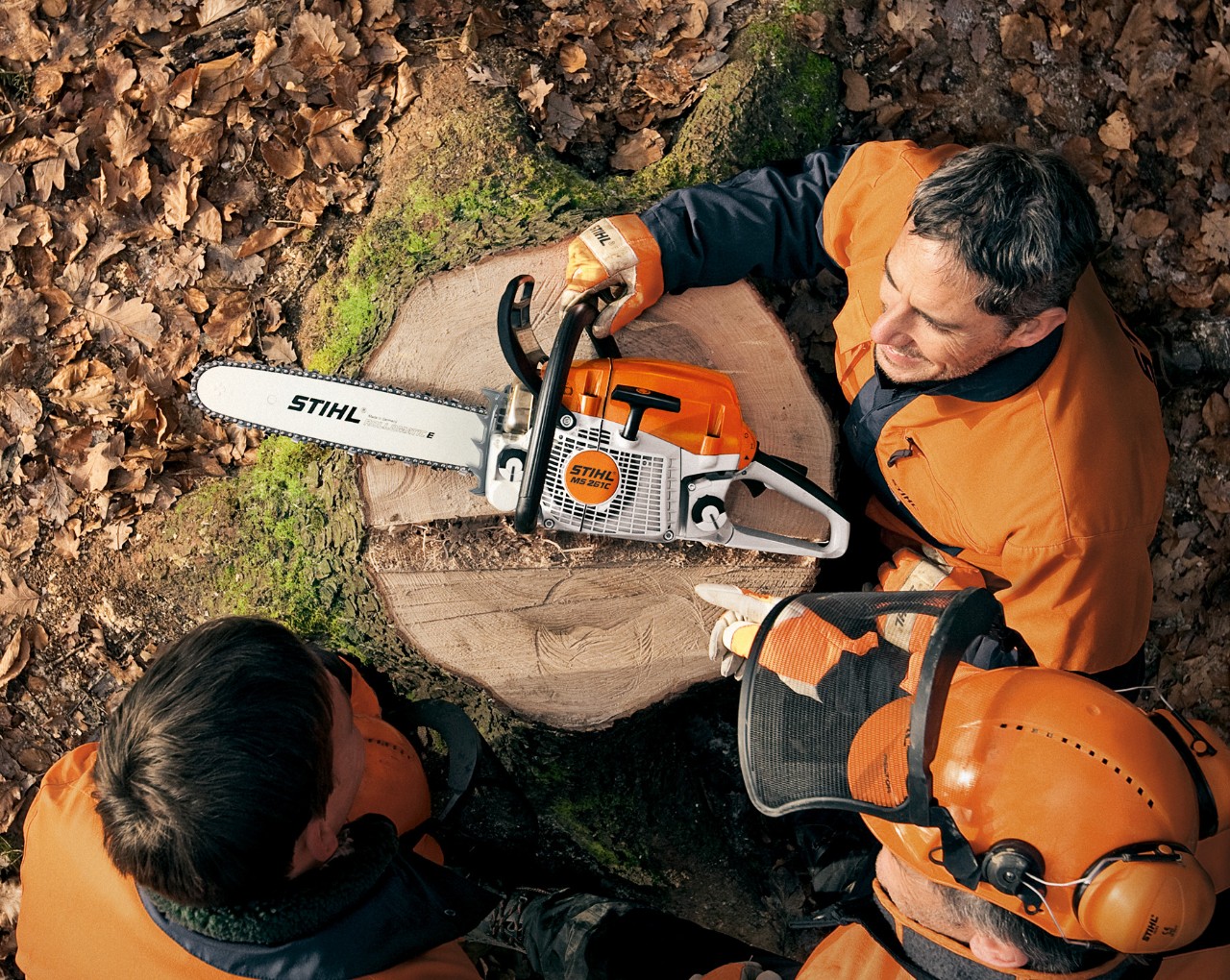 Drei Männer sitzen um eine STIHL Benzin-Kettensäge MS 261 mit werkzeuglosem Tankverschluss herum